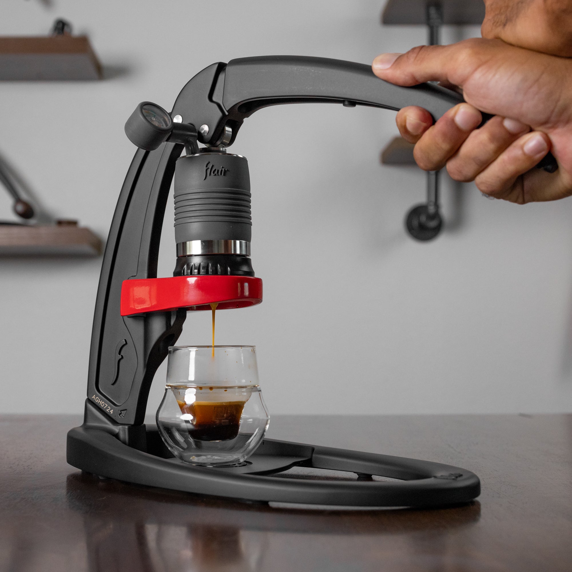 Hand pressing a coffee press with a glass of coffee below, set against a neutral background.