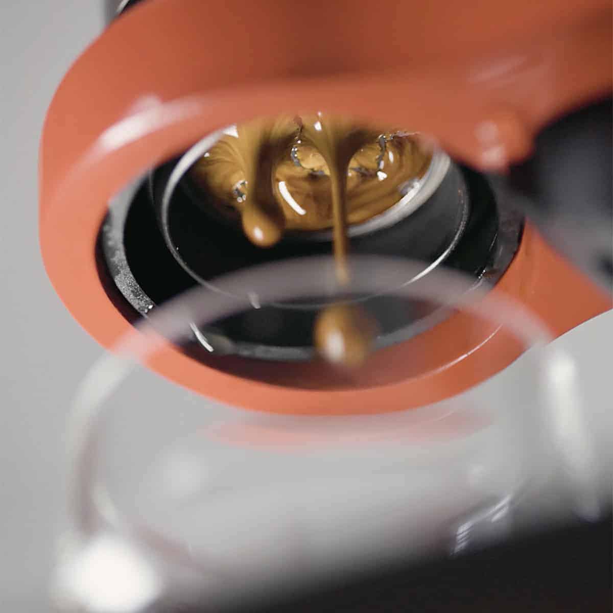 Coffee being poured from a red coffee machine into a white container.