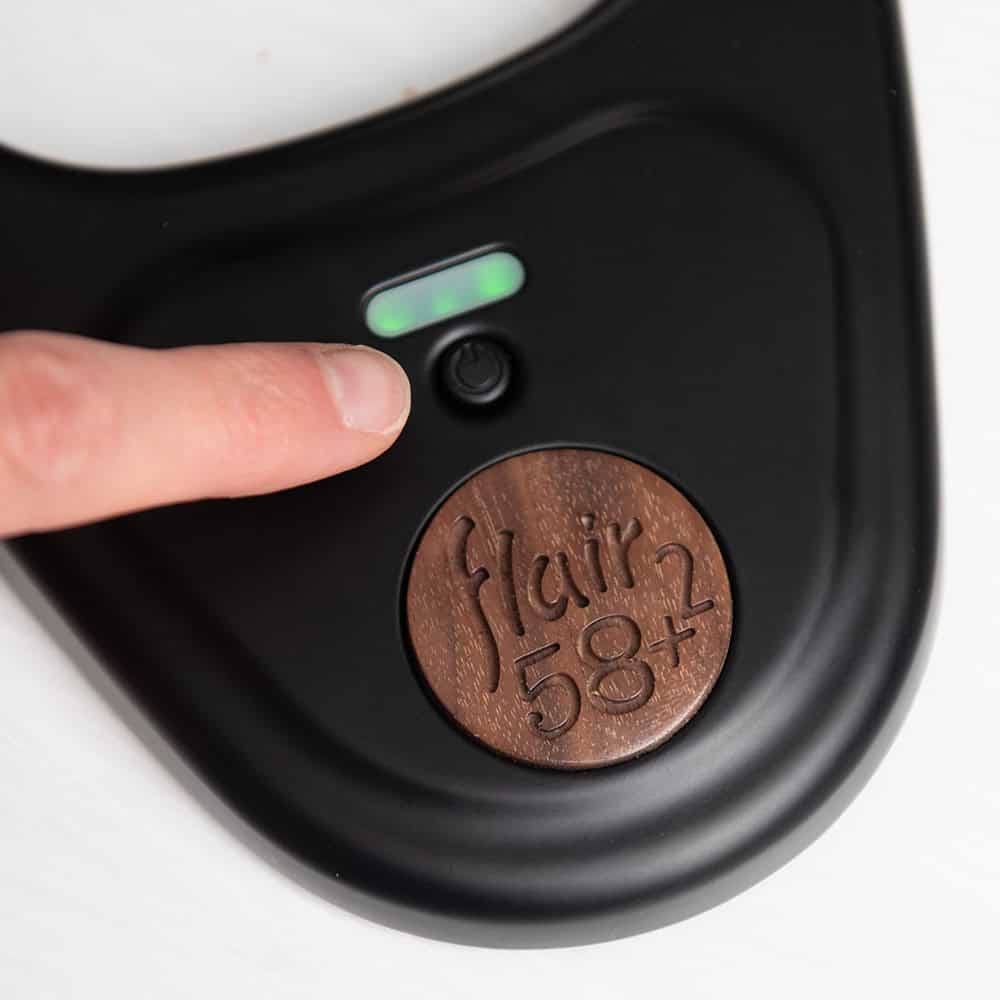 Close-up of a coffee maker with 'flair 58' branding and a finger pressing a button.