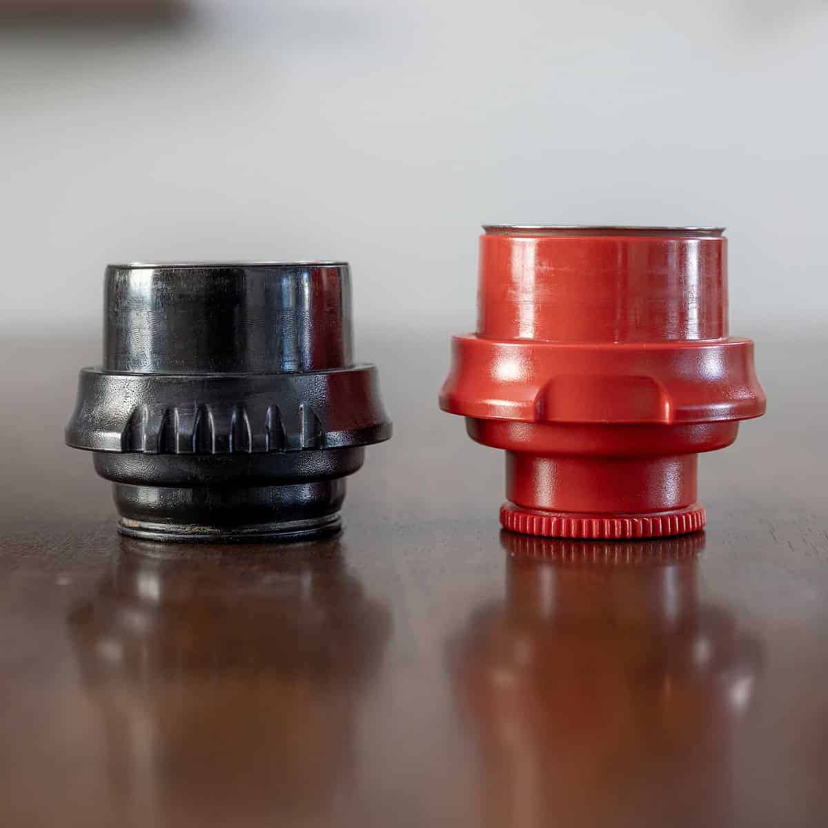 Black and red cylindrical objects on a reflective surface with a neutral background