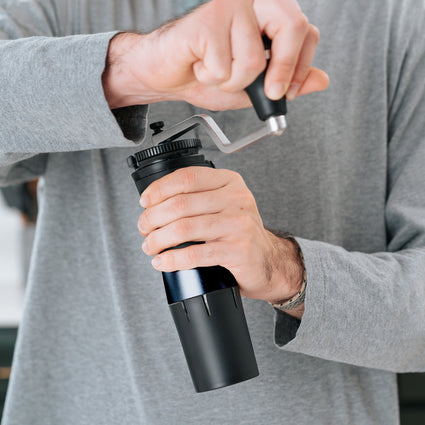 Person using a manual coffee grinder with a blurred background